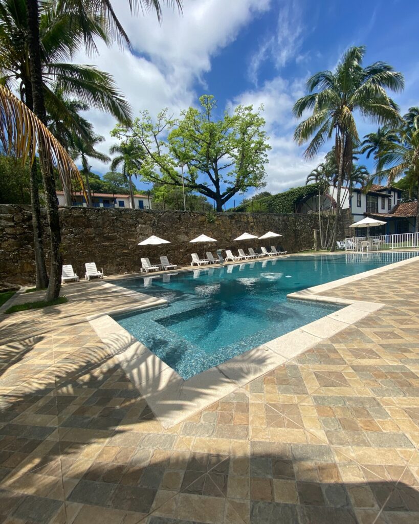 Piscina com deck de pedra rodeada por coqueiros e jardim em uma das fazendas históricas para se hospedar com lazer completo.