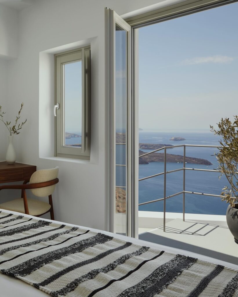 Quarto minimalista com área de trabalho e varanda com vista para o mar em hoteis boutique em santorini.