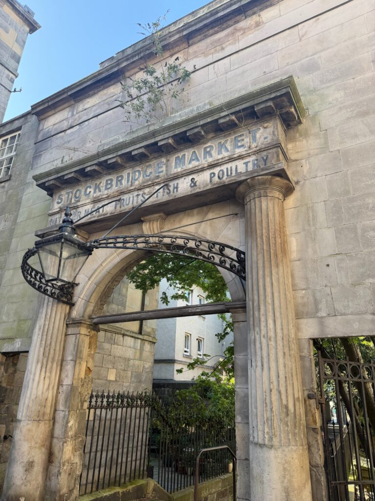 Entrada monumental em arco de pedra do Stockbridge Market, bairro Stockbridge. Dica de onde ficar em Edimburgo para uma vibe de vilarejo.