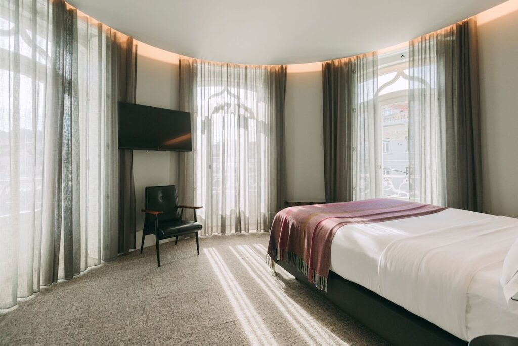 Suíte moderna com paredes curvas, janelas arqueadas e cortinas translúcidas no 1908 Lisboa Hotel, um sofisticado hotel boutique na Europa.