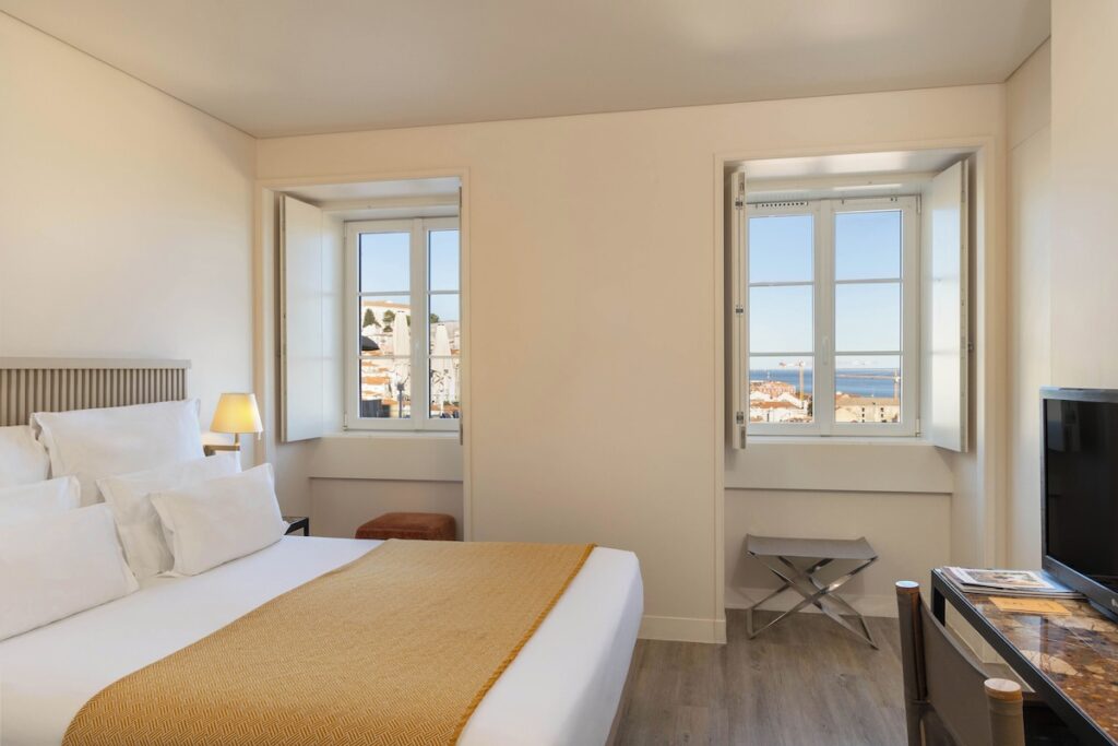 Quarto minimalista do Memmo Alfama, referência de hoteis boutique em lisboa, com manta amarela, janelas com vista da cidade e decoração clean.