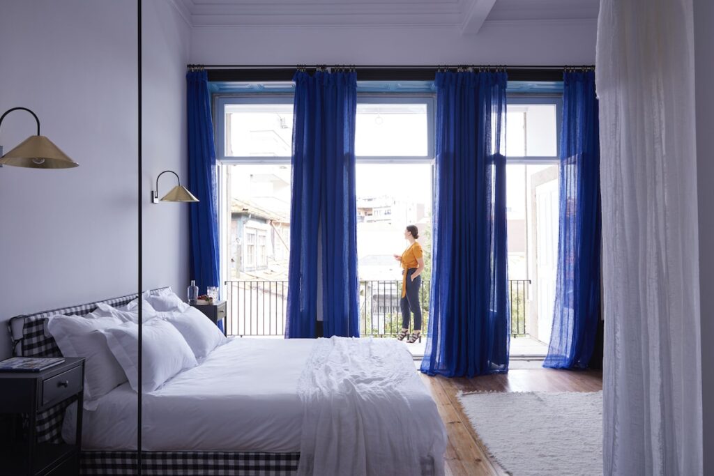 Quarto de casal com cabeceira vichy, cortinas azuis e arandelas de latão do Cocorico Luxury House, um dos charmosos hotéis boutique no Porto.