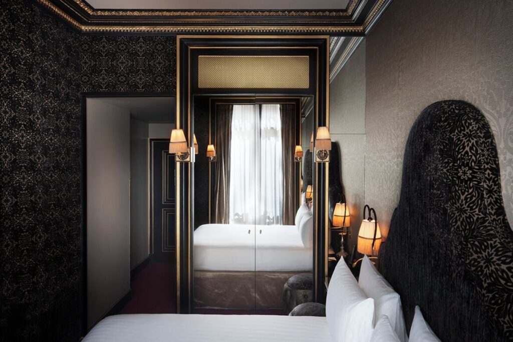 Quarto de luxo do Maison Souquet, um dos mais charmosos hoteis boutique em paris, com papel de parede adamascado escuro, espelho com moldura dourada e arandelas.