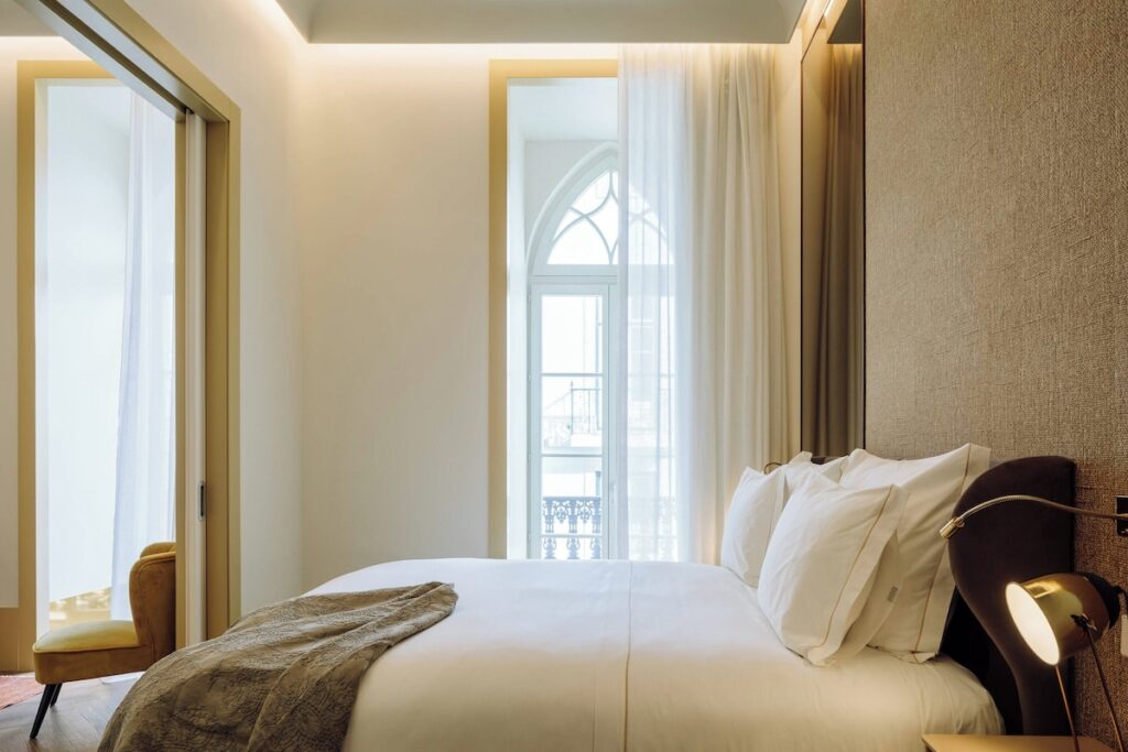 Suíte minimalista no The Ivens Hotel, um dos requintados hoteis boutique em lisboa, com cabeceira texturizada e janela em arco ogival.