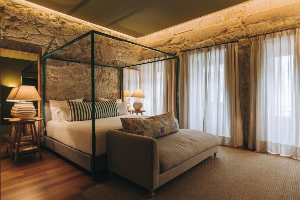 Cama de dossel sob sanca iluminada em quarto rústico com parede de pedra no Torel Saboaria, excelente opção entre hotéis boutique no Porto.