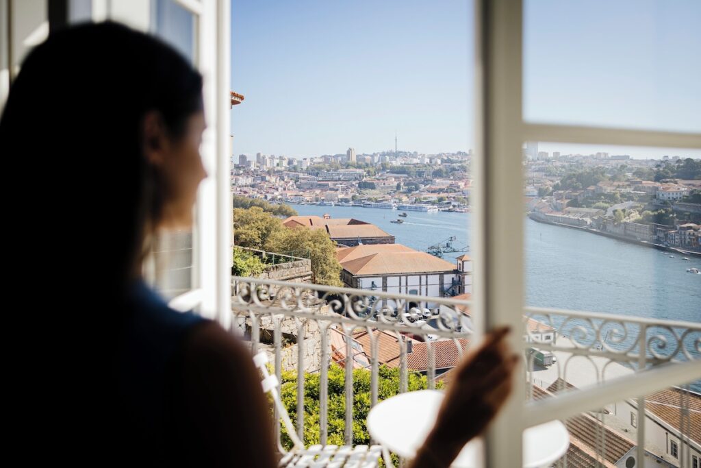 Mulher na janela de um dos hotéis boutique no Porto contemplando a vista panorâmica do Rio Douro a partir de uma varanda clássica.