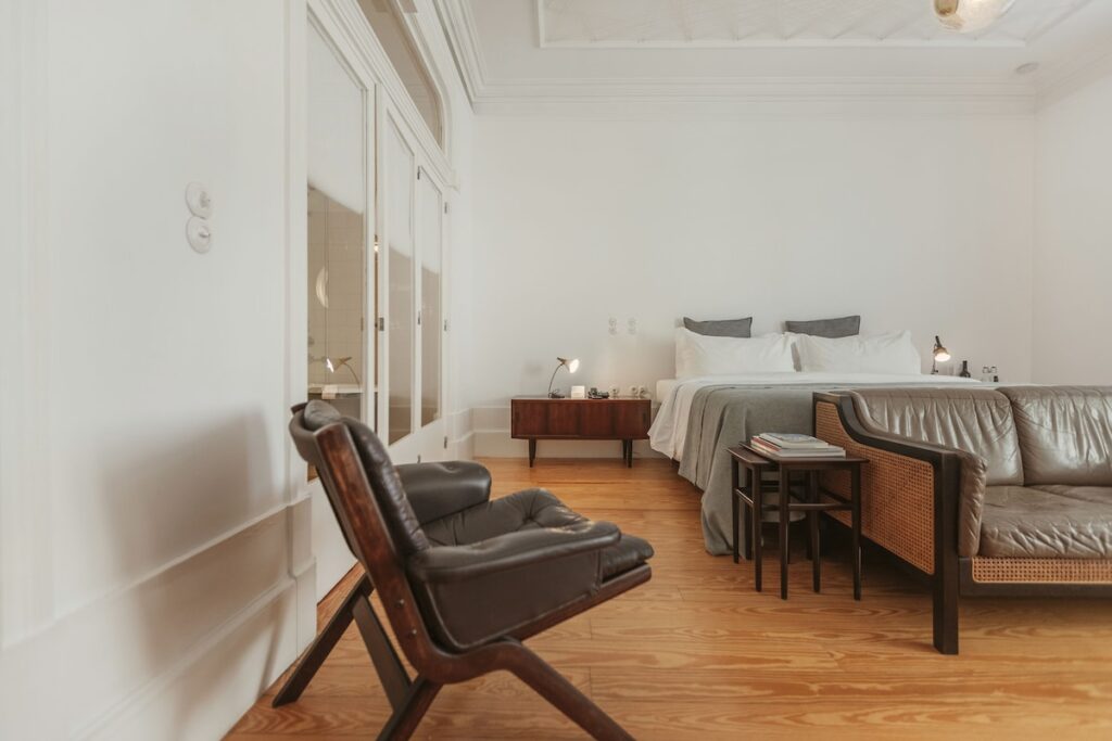Suíte de luxo em hotel boutique no Porto com piso de madeira, teto de gesso trabalhado e móveis mid-century de couro.