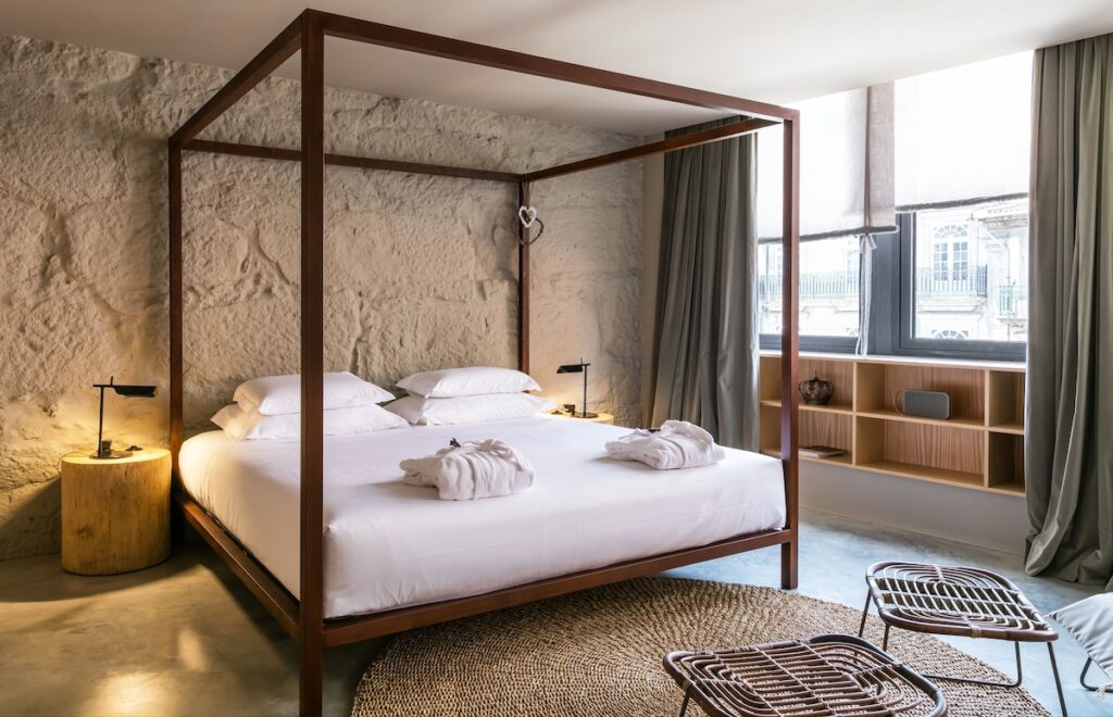 Cama de dossel em quarto com parede de pedra e tapete de fibra, destaque em um dos hotéis boutique no Porto. Foto do Armazém Luxury Housing.