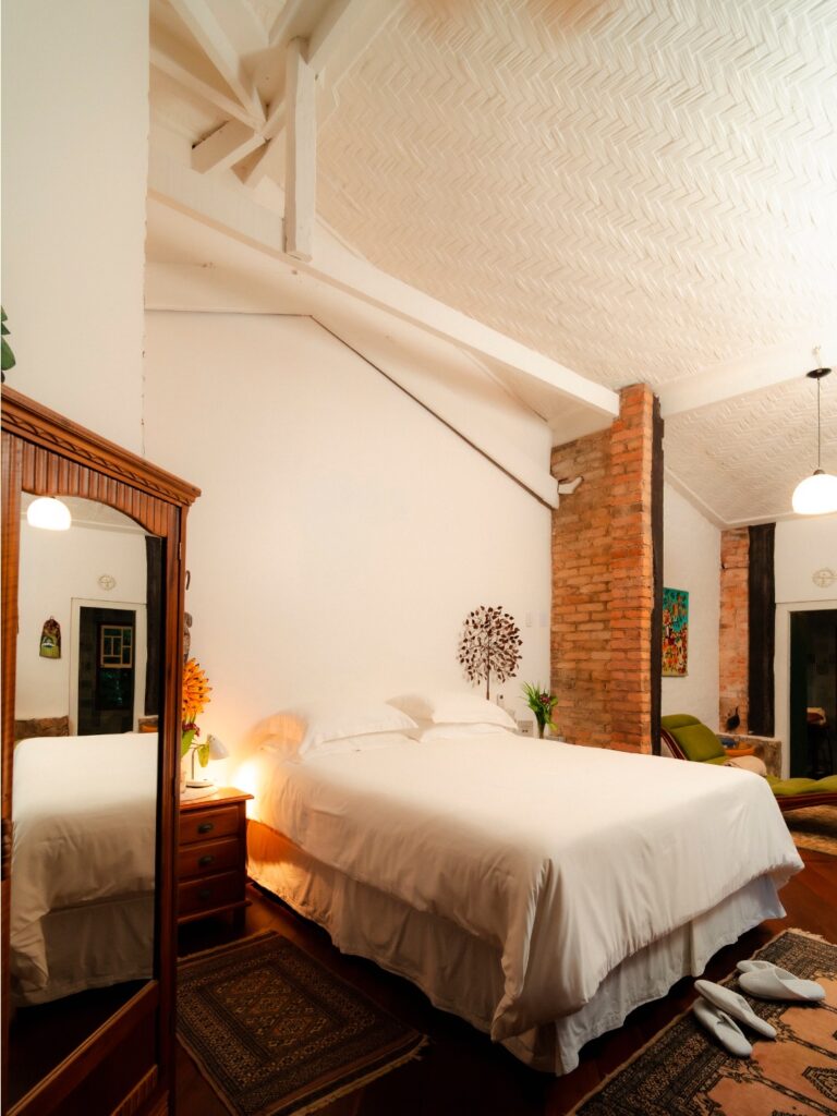 Quarto rústico e aconchegante no Ronco do Bugio, em Piedade, ideal para casais buscando hotéis românticos em São Paulo, com vigas de madeira e tijolos aparentes.