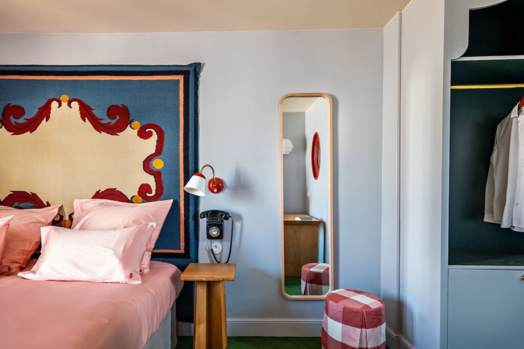 Cama com cabeceira de tapeçaria barroca azul e vermelha no Hôtel de la Boétie, um dos mais charmosos hoteis boutique em paris, com telefone vintage e espelho.
