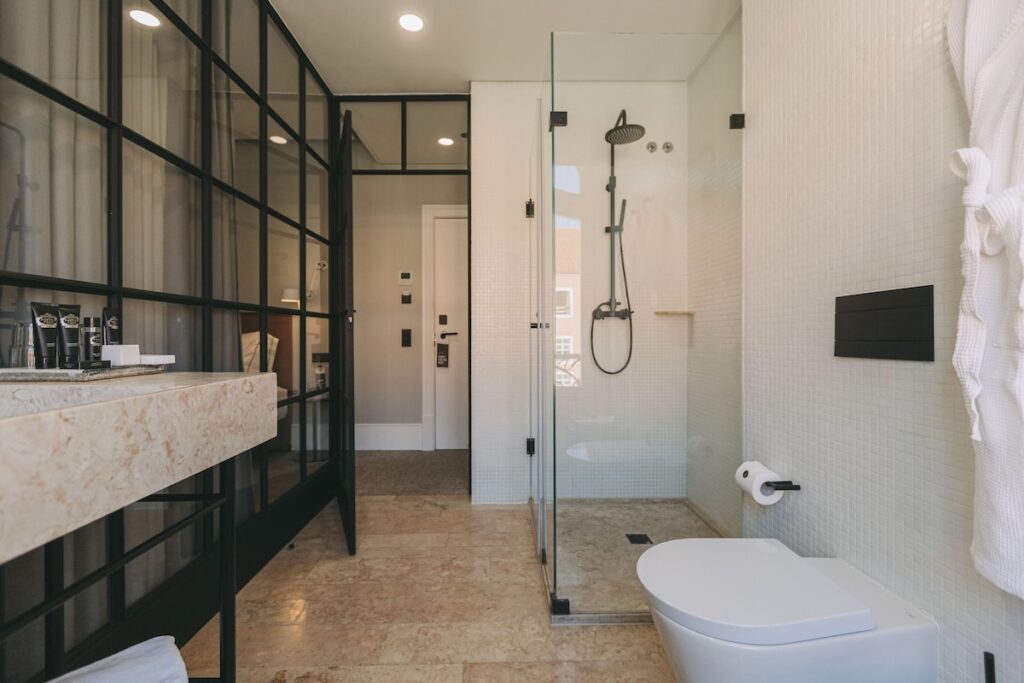 Banheiro de estilo industrial com divisória de vidro quadriculado e bancada de mármore no 1908 Lisboa Hotel, renomado hotel boutique na Europa.