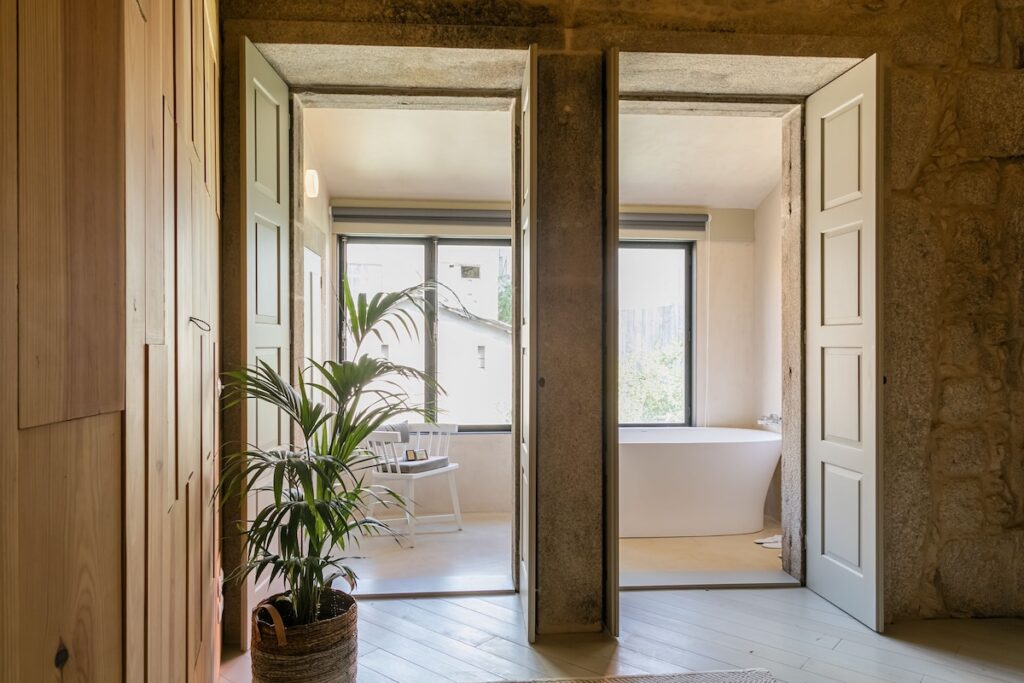 Banheira vitoriana e varanda com planta vistas através de arcos de pedra em charmosa suíte de hotel boutique no Porto. Foto do Armazém Luxury Housing.