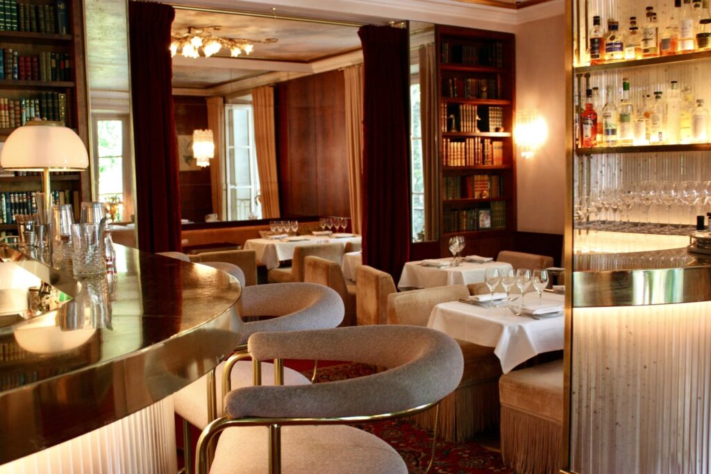 Bar e restaurante intimista com balcão de latão e estantes de livros no Hôtel Particulier Montmartre, destaque entre hoteis boutique em paris.