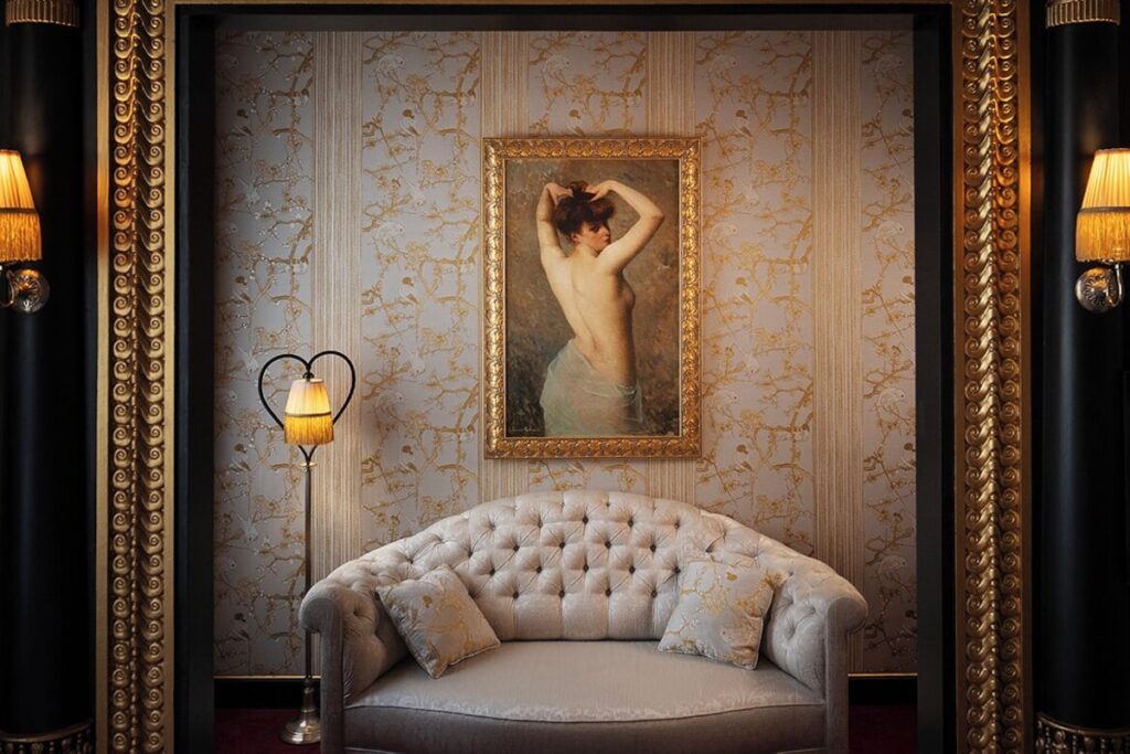 Sofá capitonê champanhe sob quadro clássico na alcova da Maison Souquet, um dos marcantes hoteis boutique em paris, com decoração boudoir.