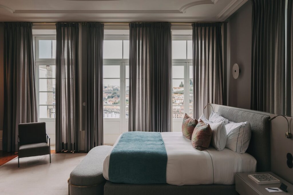 Quarto de casal sofisticado com detalhes azul-turquesa e grandes janelas clássicas, uma opção elegante de onde dormir no Porto.