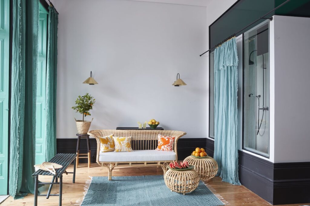Sala de estar de suíte com sofá de vime e cortinas em tons de azul em luxuoso hotel boutique no Porto, com design acolhedor e sofisticado.