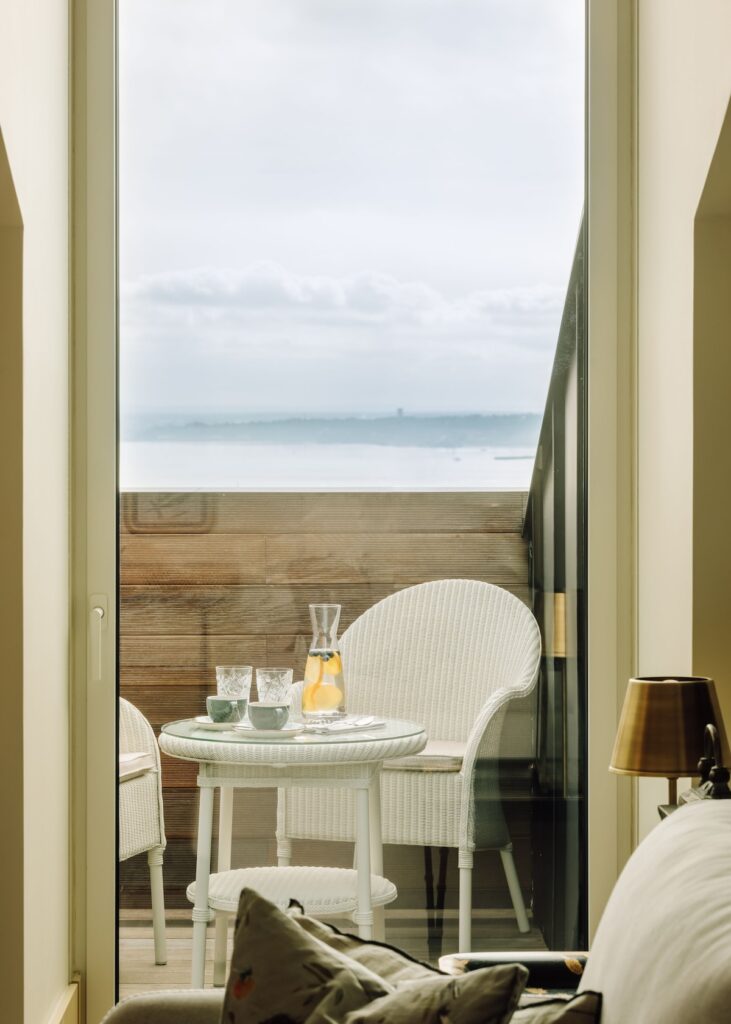 Varanda privativa de suíte no The Ivens Hotel, com conjunto de bistrô branco e vista de rio, destaque dos hoteis boutique em lisboa.