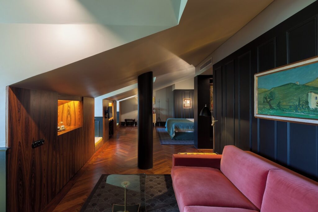 Suíte de ático no Valverde Hotel com teto inclinado, sofá rosa, painel preto e piso de madeira, destaque requintado de hoteis boutique em lisboa.