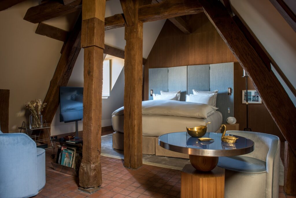 Quarto de hotel sob sótão com vigas de madeira rústica e móveis modernos no Cour des Vosges, referência de hoteis boutique em paris.