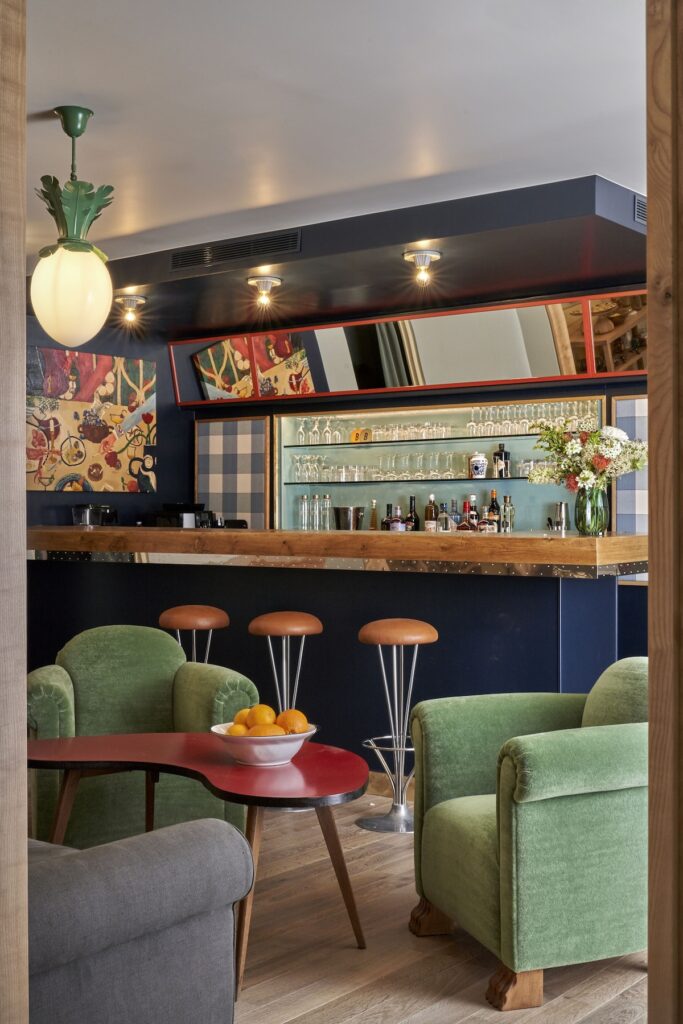 Área de bar charmosa no Hôtel de la Boétie, exemplo vibrante de hoteis boutique em paris, decorada com poltronas de veludo verde e balcão azul-escuro.