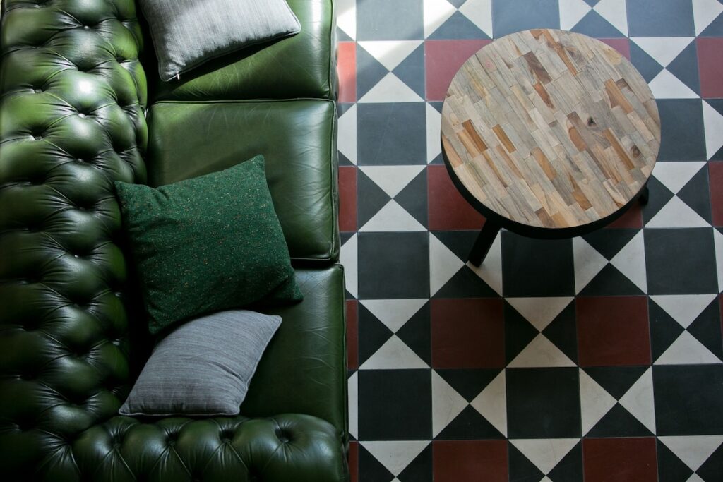 Sofá Chesterfield em couro verde sobre piso de ladrilho hidráulico geométrico no 1908 Lisboa Hotel, elegante hotel boutique na Europa.