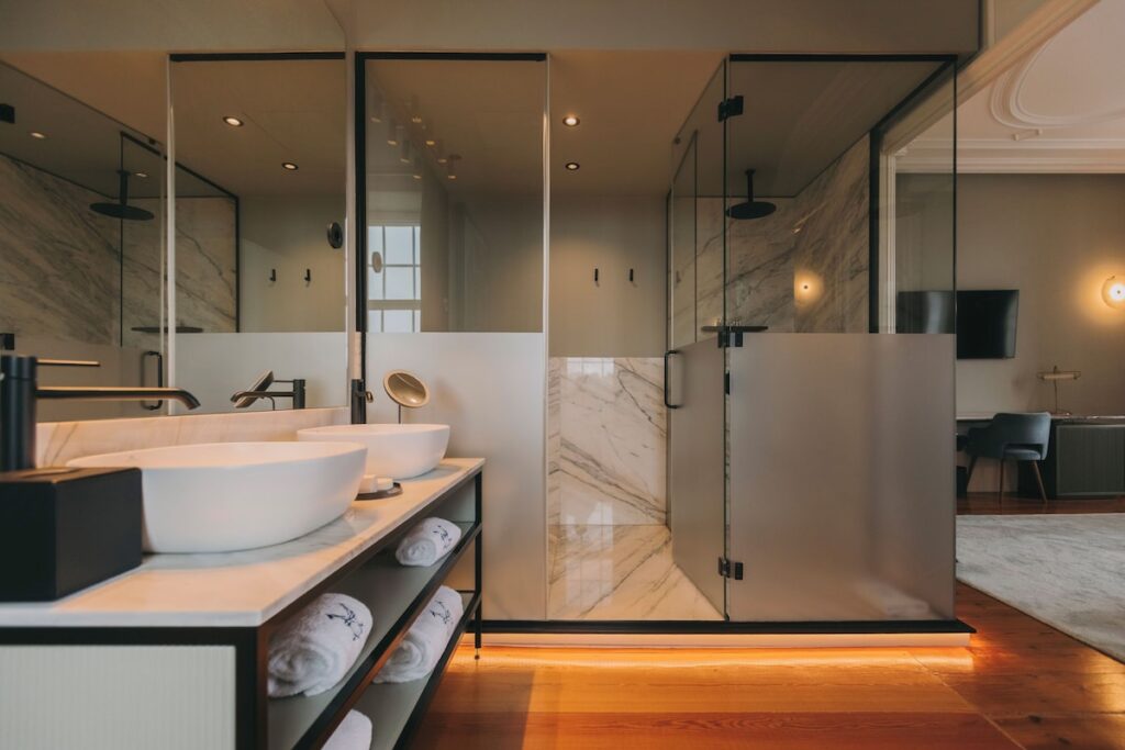 Banheiro contemporâneo com pia dupla de mármore Carrara e detalhes pretos em suíte luxuosa de hotel boutique no Porto.