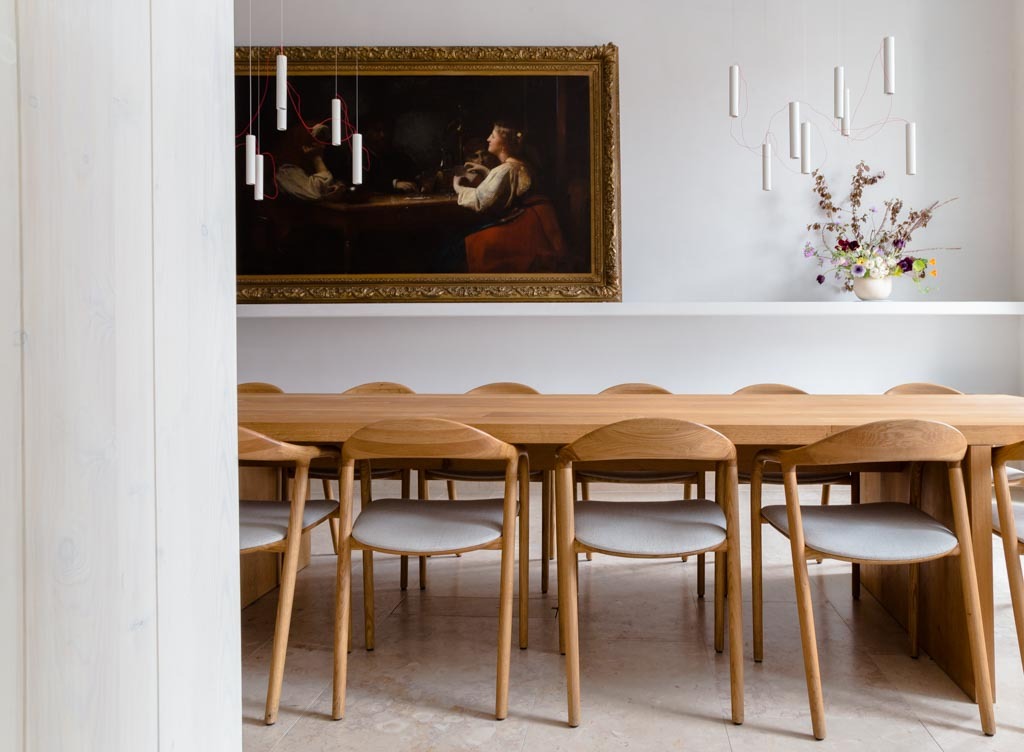 Sala de jantar comunitária no Santa Clara 1728 com mesa de madeira clara, cadeiras curvas e pintura clássica, charme em hoteis boutique em lisboa.