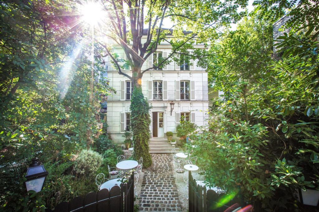 Fachada histórica e pátio ajardinado com mesas ao ar livre no Hôtel Particulier Montmartre, joia escondida dos hoteis boutique em paris.