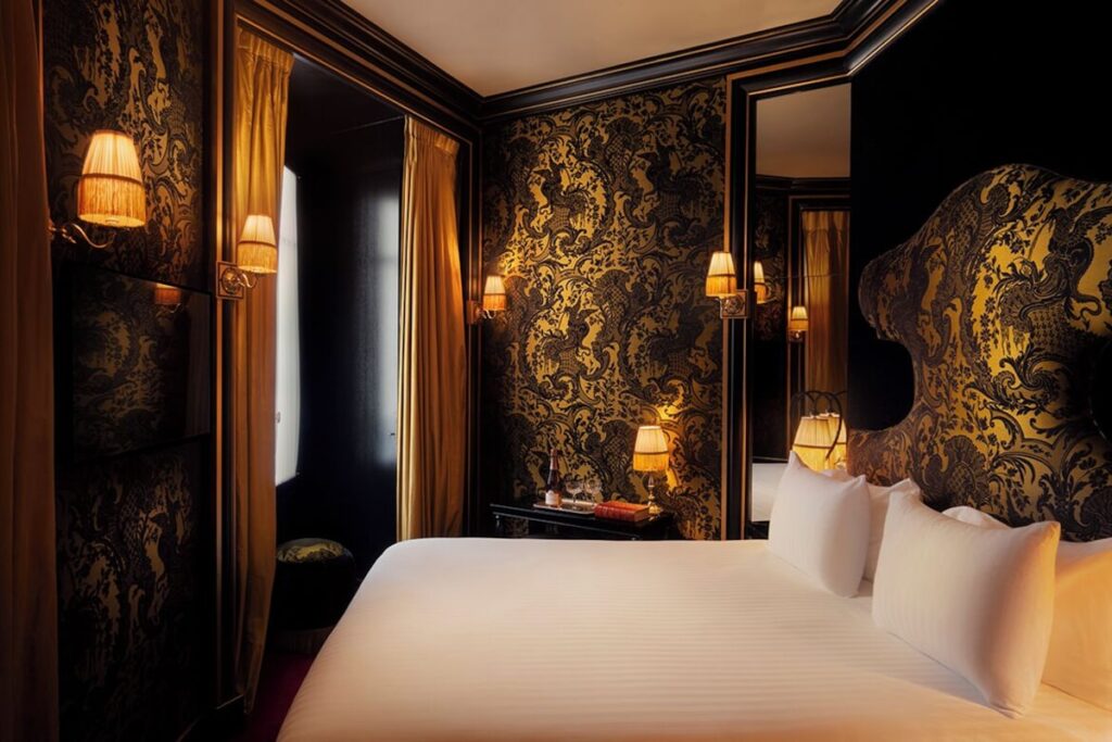 Quarto luxuoso da Maison Souquet, ícone dos hoteis boutique em paris, com papel de parede dourado e preto, cabeceira escultural e iluminação âmbar.