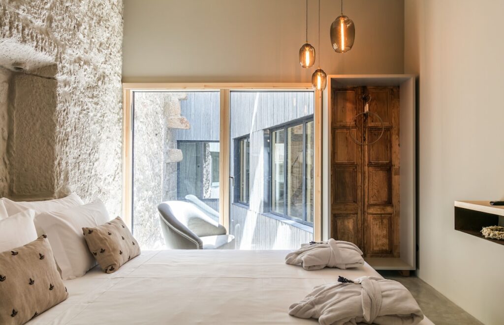Quarto de casal iluminado com parede de pedra e pendentes de vidro, uma elegante opção de onde dormir no Porto. Foto do Armazém Luxury Housing.