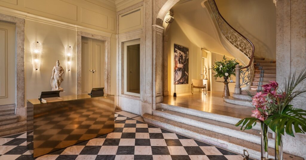 Lobby de entrada do Verride Palácio Santa Catarina com balcão dourado, escada de mármore e piso xadrez, sofisticação em hoteis boutique em lisboa.