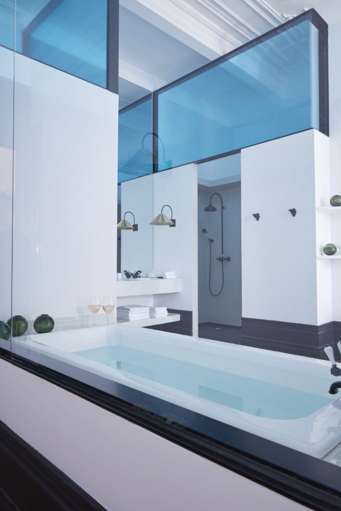Banheiro integrado com banheira e divisória de vidro azul no Cocorico Luxury House, referência de onde dormir no Porto com design moderno.