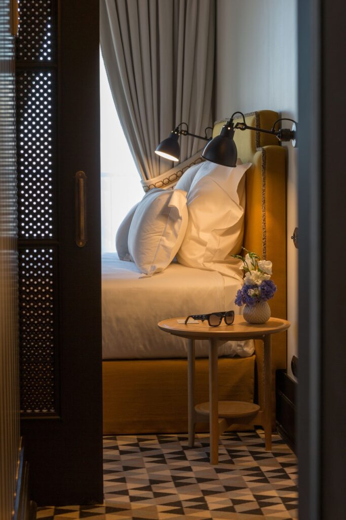 Detalhe aconchegante de quarto no Valverde Hotel com cabeceira ocre, arandelas pretas e mesa de cabeceira, charme em hoteis boutique em lisboa.