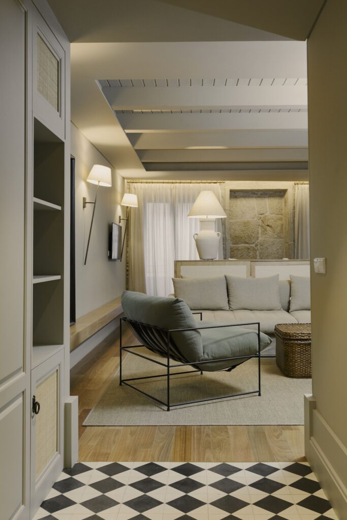 Sala de estar com sofá bege e poltrona verde em frente a parede de pedra no hotel boutique no Porto Torel Saboaria.