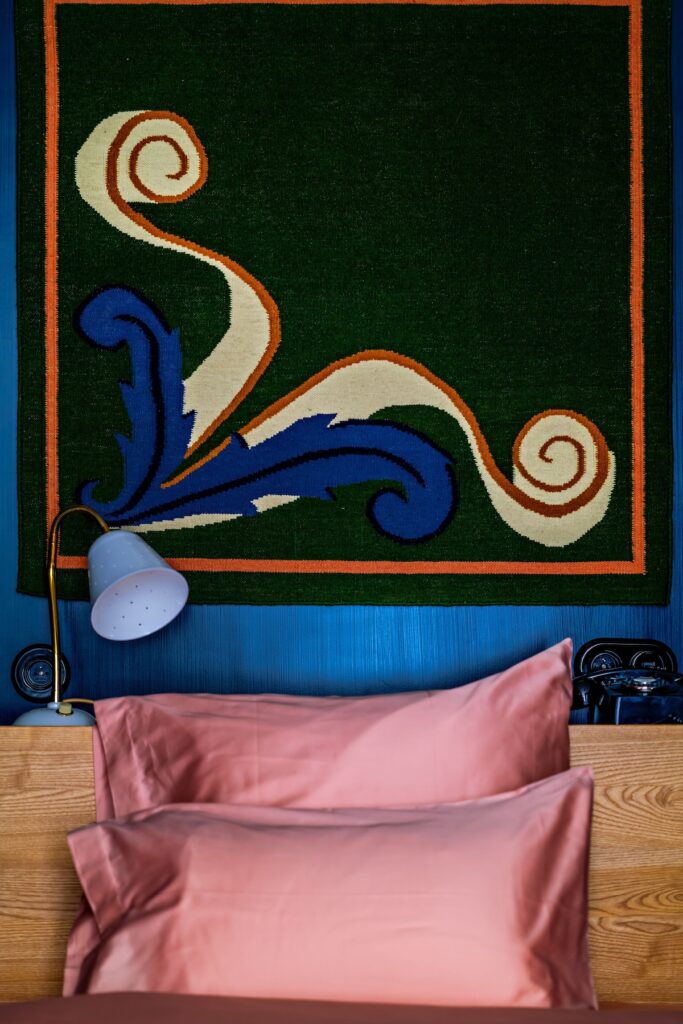 Detalhe de cama do Hôtel de la Boétie, destaque de hoteis boutique em paris, com cabeceira de madeira, lençóis rosa e tapeçaria verde e azul na parede.