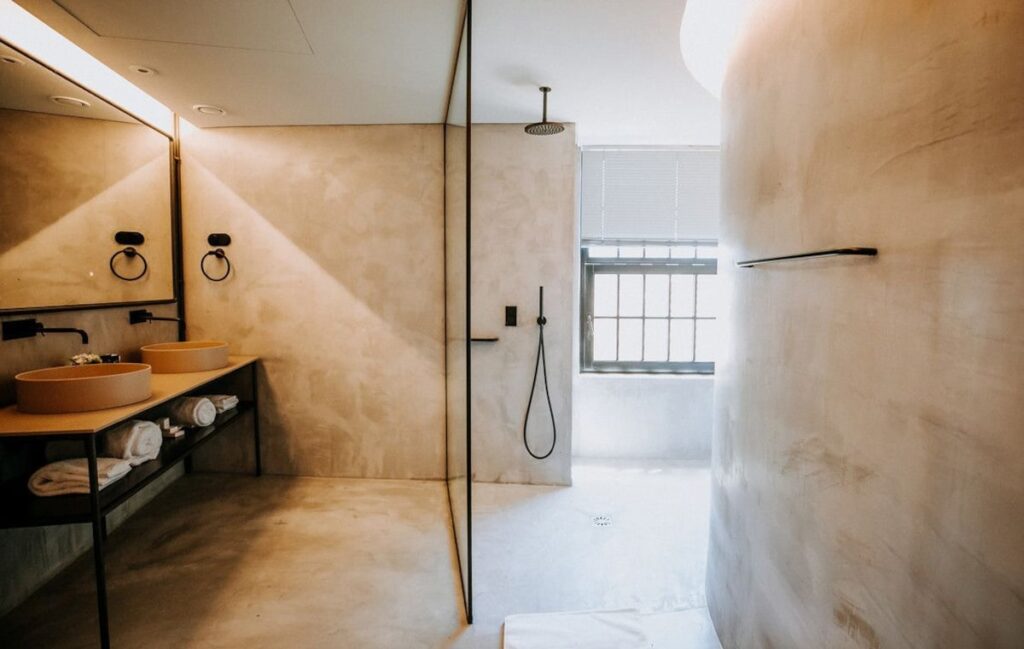Banheiro minimalista de design com revestimento em microcimento areia, cubas terracota e detalhes pretos em sofisticado hotel boutique no Porto.