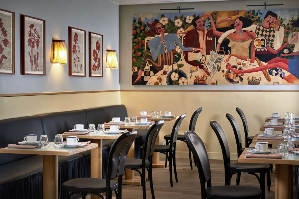 Salão de refeições do Hôtel de la Boétie, referência entre os hoteis boutique em paris, com mesas postas, bancos de couro preto e uma grande tela colorida.