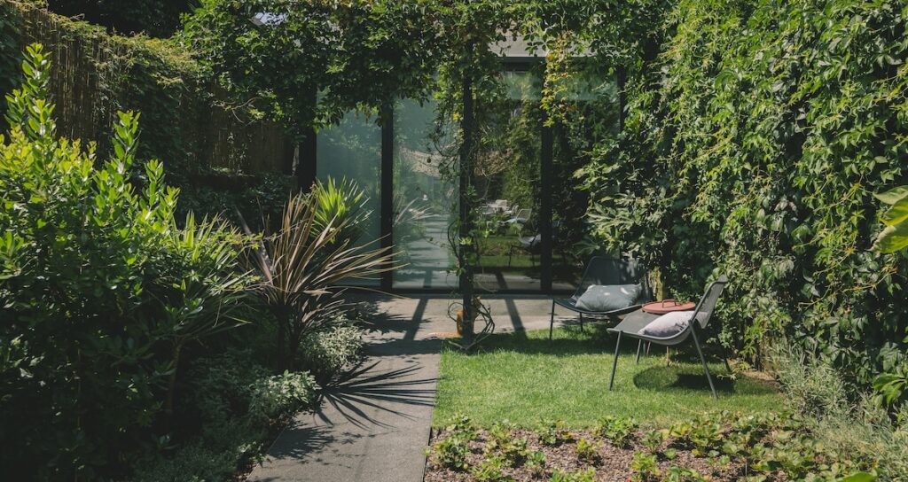 Jardim interno com muito verde, cadeiras lounge e pergolado em hotel boutique no Porto, criando um oásis urbano relaxante.