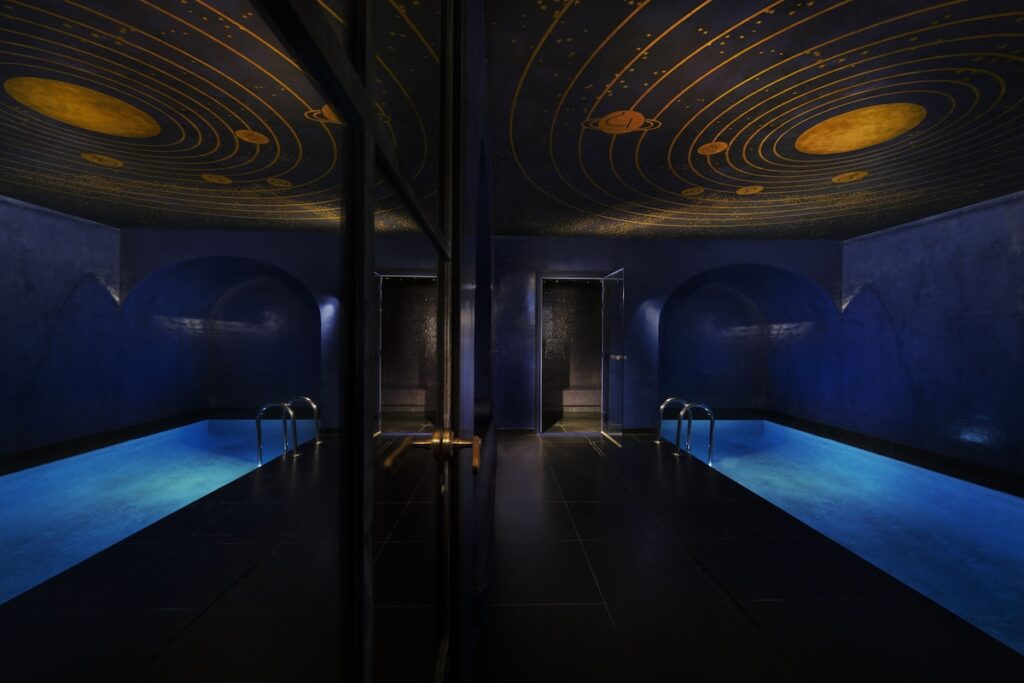 Piscina coberta do spa da Maison Souquet, entre os melhores hoteis boutique em paris, com teto pintado com o sistema solar e iluminação azul.