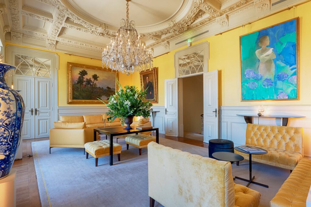 Sala Amarela no Verride Palácio Santa Catarina com teto de estuque ornamentado, lustre de cristal e sofás mostarda, joia dos hoteis boutique em lisboa.