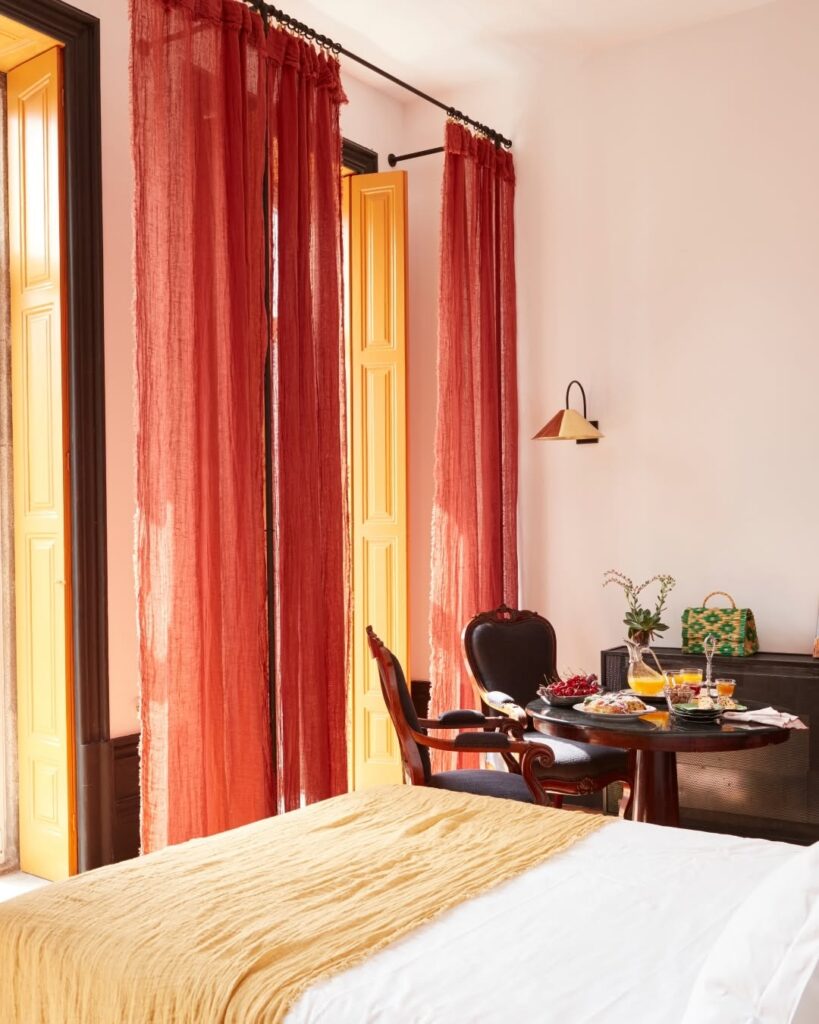 Quarto com mesa de café da manhã, cortinas terracota e portas amarelas no Cocorico Luxury House, destaque entre os hotéis de charme no Porto.