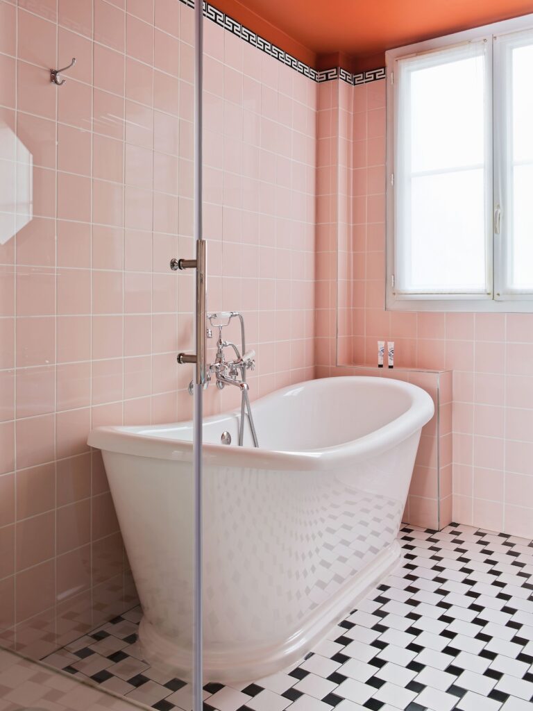 Banheiro retrô com azulejos rosa, teto terracota e banheira branca no Hôtel Les Deux Gares, um destaque entre os hoteis boutique em paris.