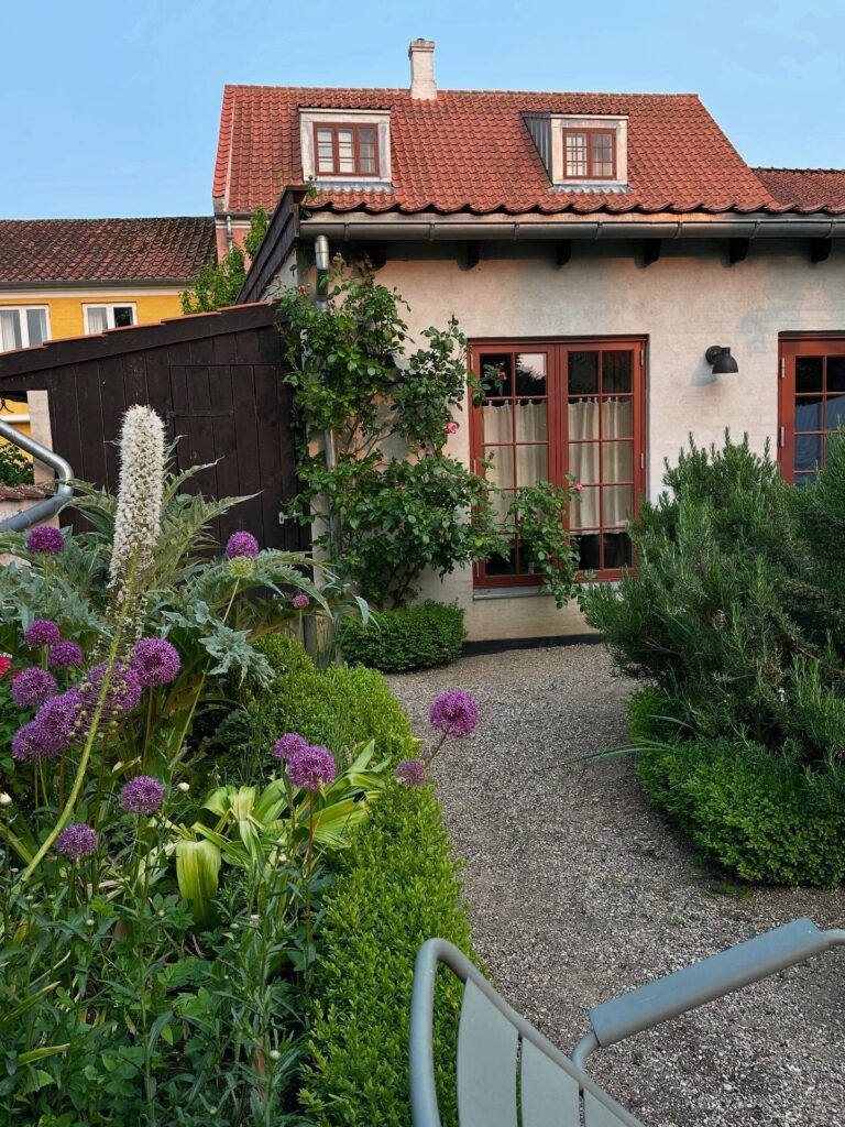 Pátio e jardim florido secreto com arbustos e flores roxas no The Monica, refúgio de lua de mel na europa.