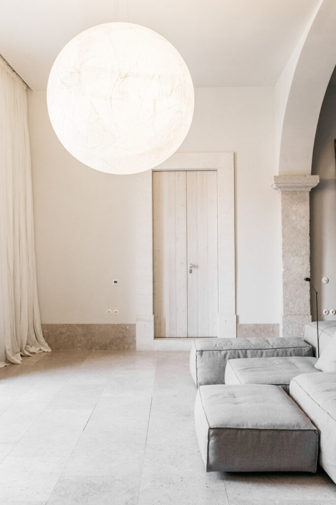 Sala de estar minimalista no Santa Clara 1728 com grande luminária esférica, sofá cinza e piso de pedra, referência de hoteis boutique em lisboa.
