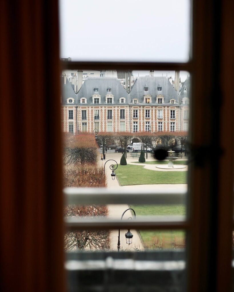 Vista enquadrada da histórica Place des Vosges através da janela do Cour des Vosges, joia dos hoteis boutique em paris.