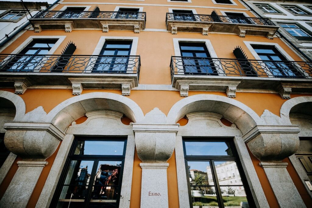 Fachada histórica restaurada com arcos de granito e paredes ocre de charmoso hotel boutique no Porto, localizado na tradicional região da Ribeira.