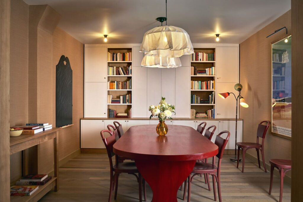 Biblioteca do Hôtel de la Boétie, ícone entre hoteis boutique em paris, com grande mesa de jantar oval vermelha, cadeiras clássicas e paredes de palha.