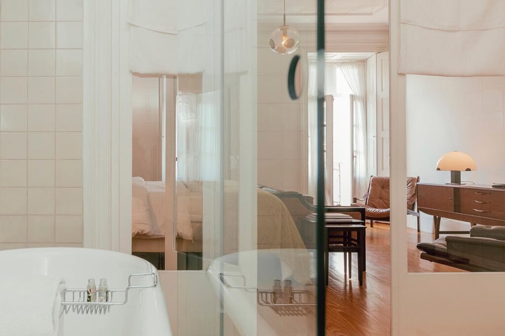 Integração visual de banheiro e quarto com móveis vintage de madeira e couro em um dos hotéis de charme no Porto.