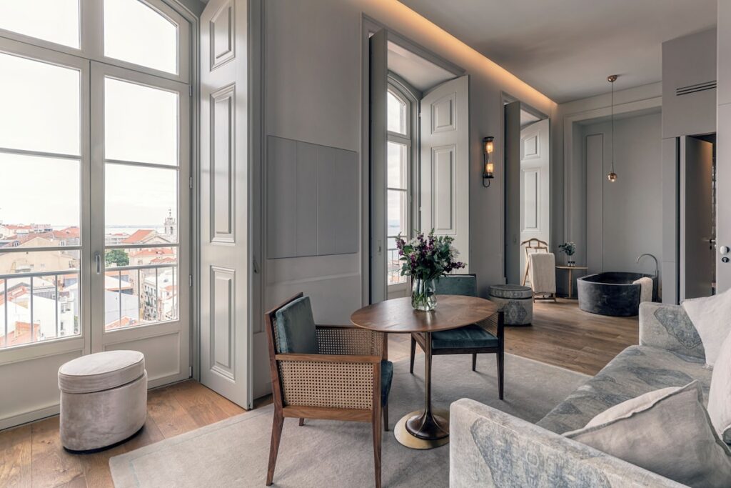 Suíte Premium no Verride Palácio Santa Catarina com banheira de pedra, mesa de jantar e sofá cinza, destaque luxuoso de hoteis boutique em lisboa.