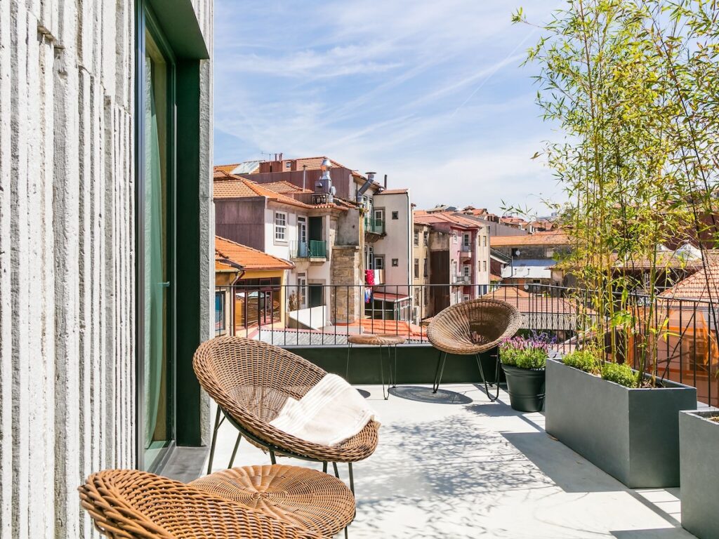 Terraço ensolarado com cadeiras de vime e plantas com vista dos telhados, opção em hotéis boutique no Porto. Foto do Armazém Luxury Housing.